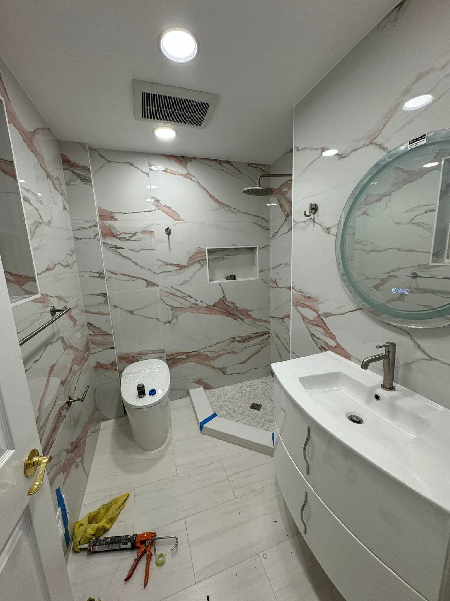 Wykończona łazienka w Bydgoszczy z marmurowymi płytkami, okrągłym lustrem z podświetleniem LED i nowoczesną umywalką. Widoczne narzędzia glazurnicze.