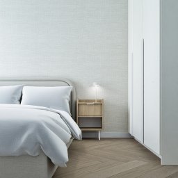 Studio projektowania wnętrz - Kwadrat na miarę - Jasna sypialnia w stylu skandynawskim: łóżko z szarą ramą, drewniana szafka nocna z lampką, parkiet w jodełkę i biała szafa w zabudowie.