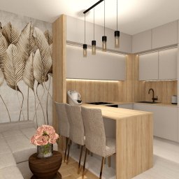 Marmoris Design - Beżowa kuchnia z wyspą i dekoracyjną tapetą w liście. Nad wyspą wiszą cztery lampy. Obok sofy stoi stolik z kwiatami. Całość w ciepłych, stonowanych barwach.