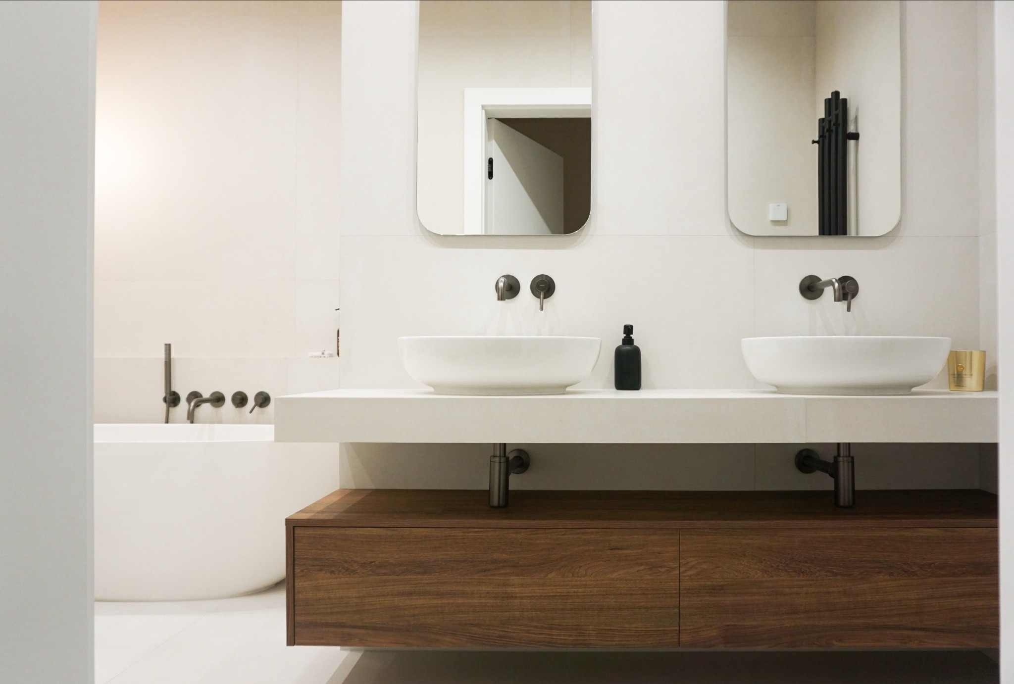 Nowoczesna łazienka z dwoma umywalkami nablatowymi, drewnianą szafką pod umywalką i minimalistyczną armaturą w kolorze grafitu. W tle widoczna wanna.