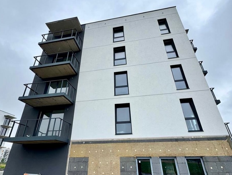 Nowoczesny budynek z balkonami z czarnymi, metalowymi barierkami i szklanymi panelami, widziany z dołu pod kątem, z widoczną izolacją na dole.