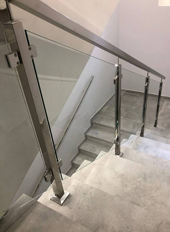 Nowoczesne schody z balustradą ze szkła i stali nierdzewnej. Minimalistyczny design, jasne wnętrze, widok z góry na stopnie. Metalowe mocowania szkła.