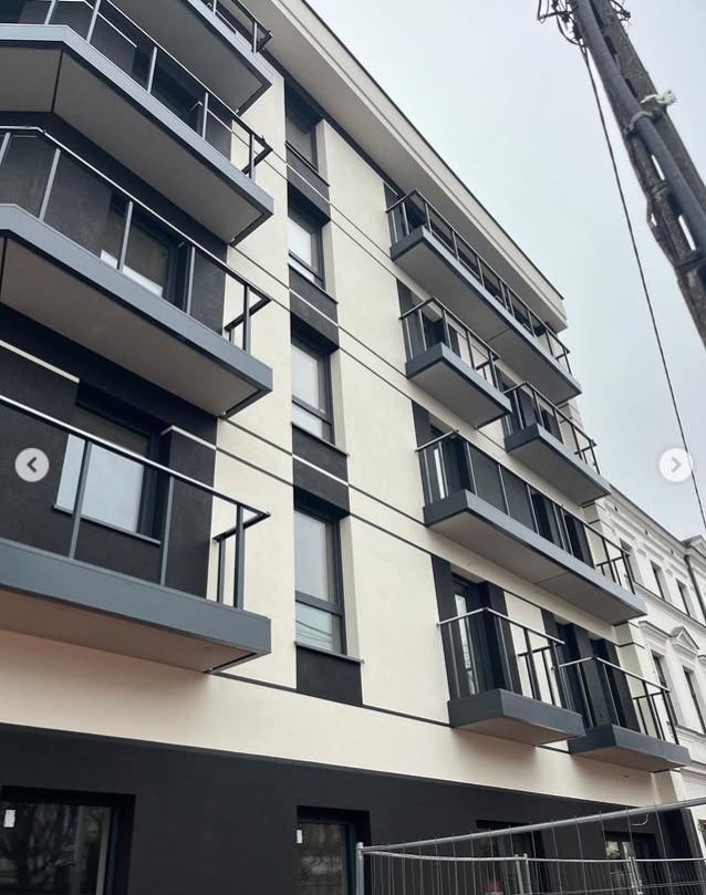 Nowoczesny budynek z balkonami i balustradami ze stali nierdzewnej, widok z dołu, pochmurne niebo w tle. Minimalistyczny design.