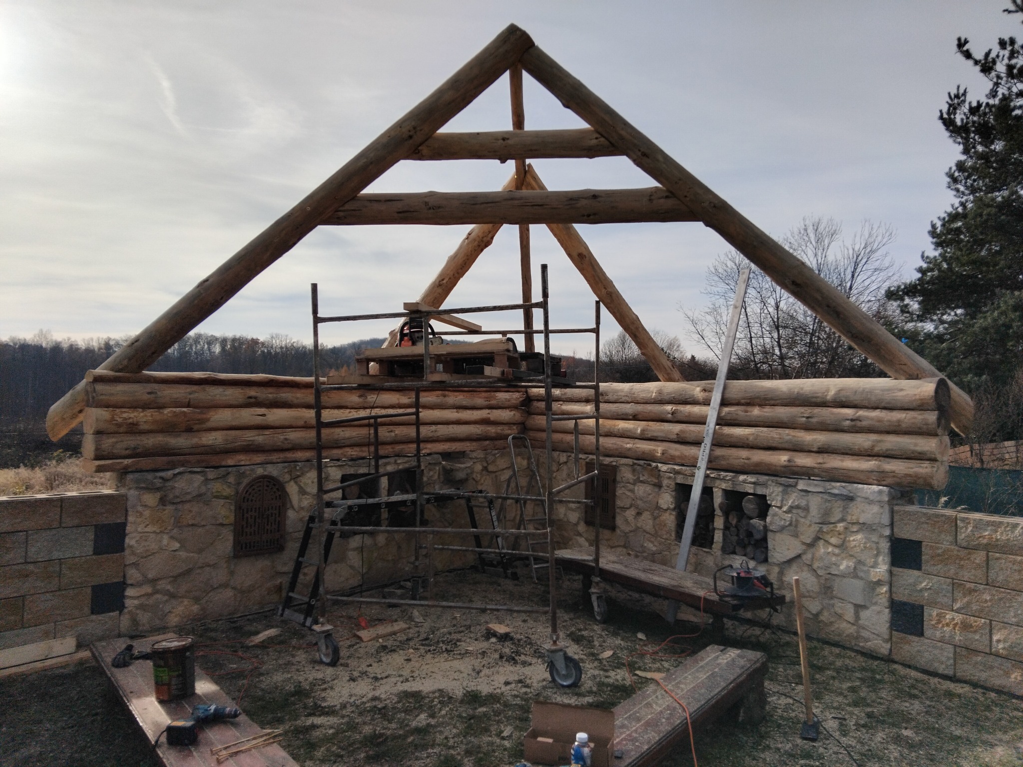 Budowa domu z bali i kamienia w Częstochowie. Widoczne rusztowania, narzędzia i elementy konstrukcyjne. Charakterystyczne połączenie drewna i kamienia.