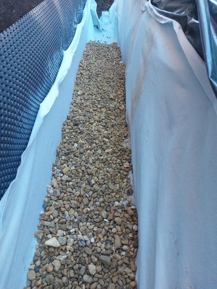 Drenaż: żwir w wykopie wyłożonym geowłókniną i folią kubełkową. Widok z góry na gotowy system odprowadzający wodę.