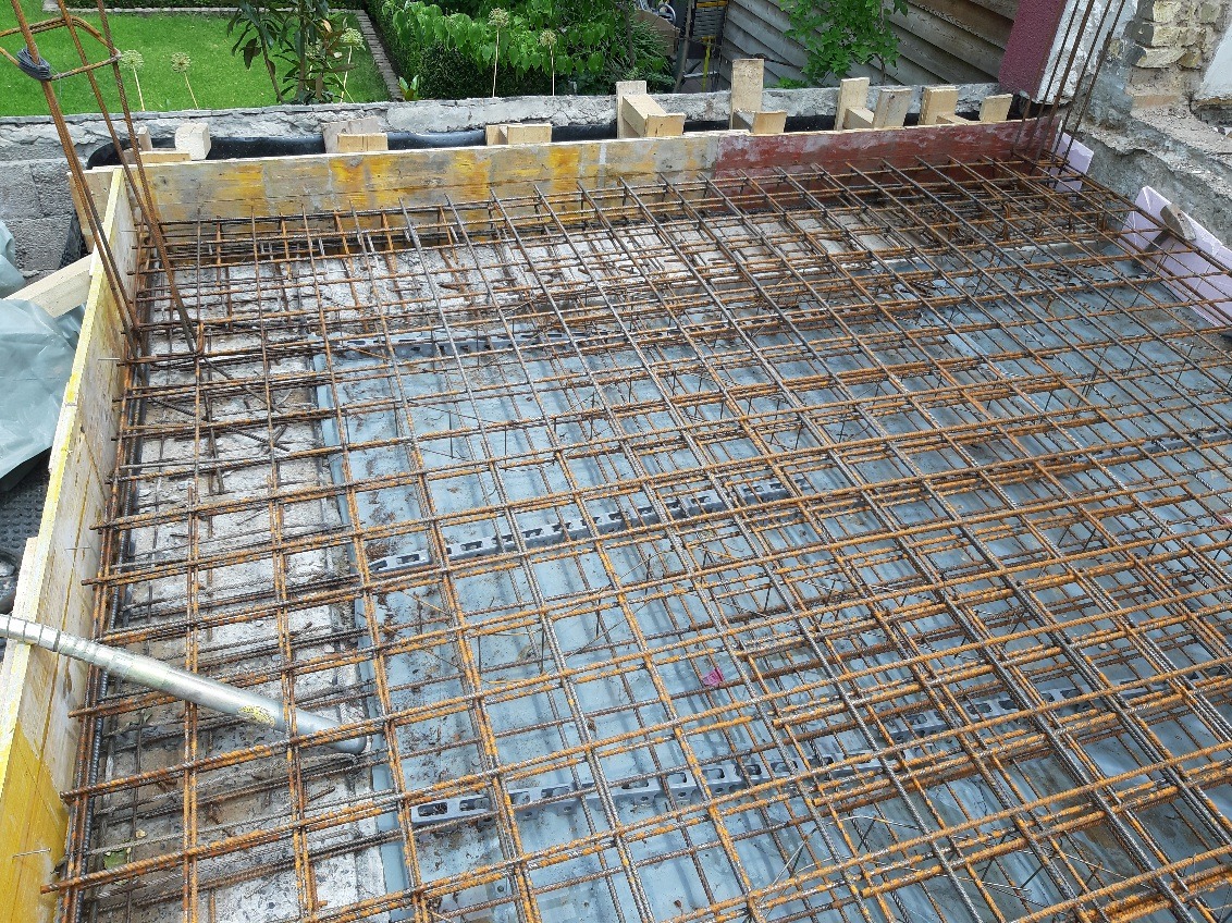 Zbrojenie płyty fundamentowej w szalunku, widoczne elementy dystansowe i wibrator do betonu. Przygotowanie do wylewania betonu na budowie.