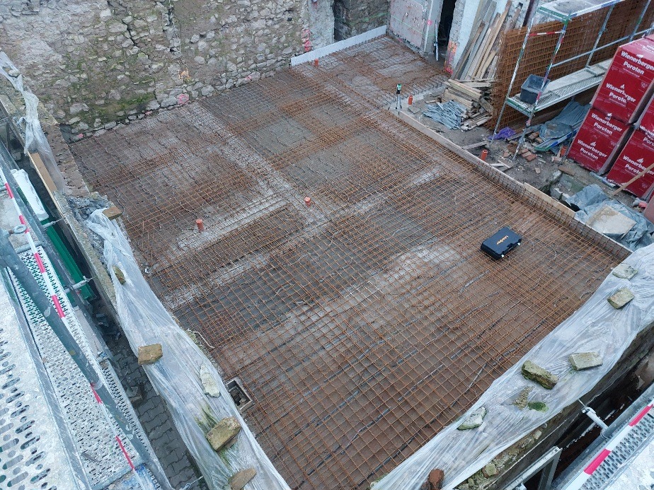 Zbrojenie płyty fundamentowej z widocznym laserowym niwelatorem, cegły Poroton w tle. Widok z góry na przygotowany teren pod wylewkę.