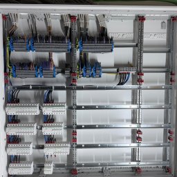 ElektroSquad Krystian Składan - Rozdzielnica elektryczna w trakcie montażu: widoczne szyny DIN, listwy zaciskowe, przewody i zabezpieczenia. Estetyczne ułożenie kabli wewnątrz skrzynki.