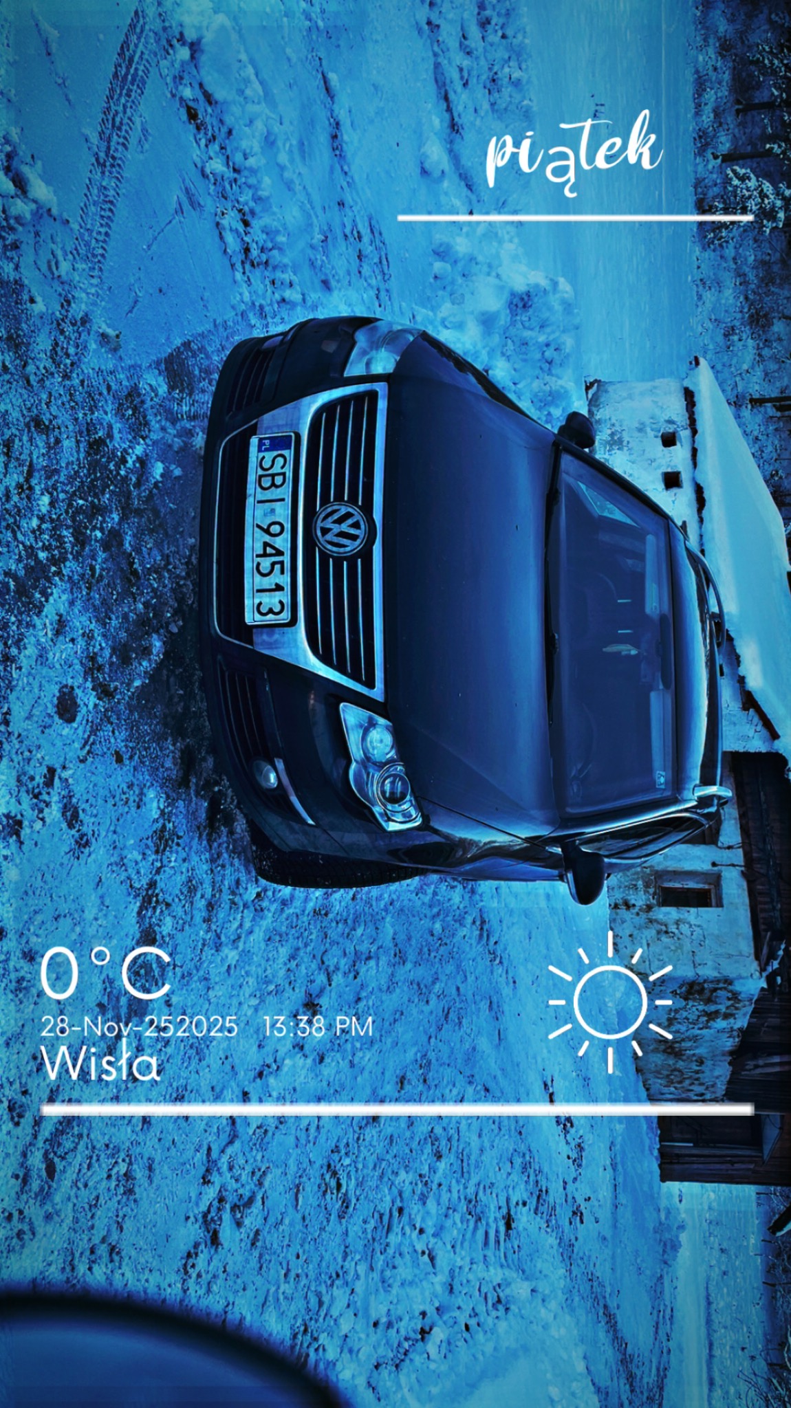 Czarny samochód osobowy marki Volkswagen na tle ośnieżonego terenu i budynku. Widoczne ślady opon na śniegu. Zdjęcie obrócone o 90 stopni.