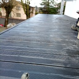 Jagiellońska 111 - Ciemnoszary taras kompozytowy z widoczną fakturą desek, fragment drabiny w tle, częściowo widoczne buty montera. Ujęcie z niskiej perspektywy.