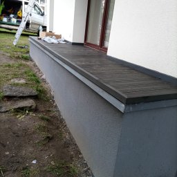 Jagiellońska 111 - Wykończony taras kompozytowy przy oknie budynku z białą elewacją. Widoczne szare wykończenie ściany i elementy montażowe. W tle drabina i samochód dostawczy.