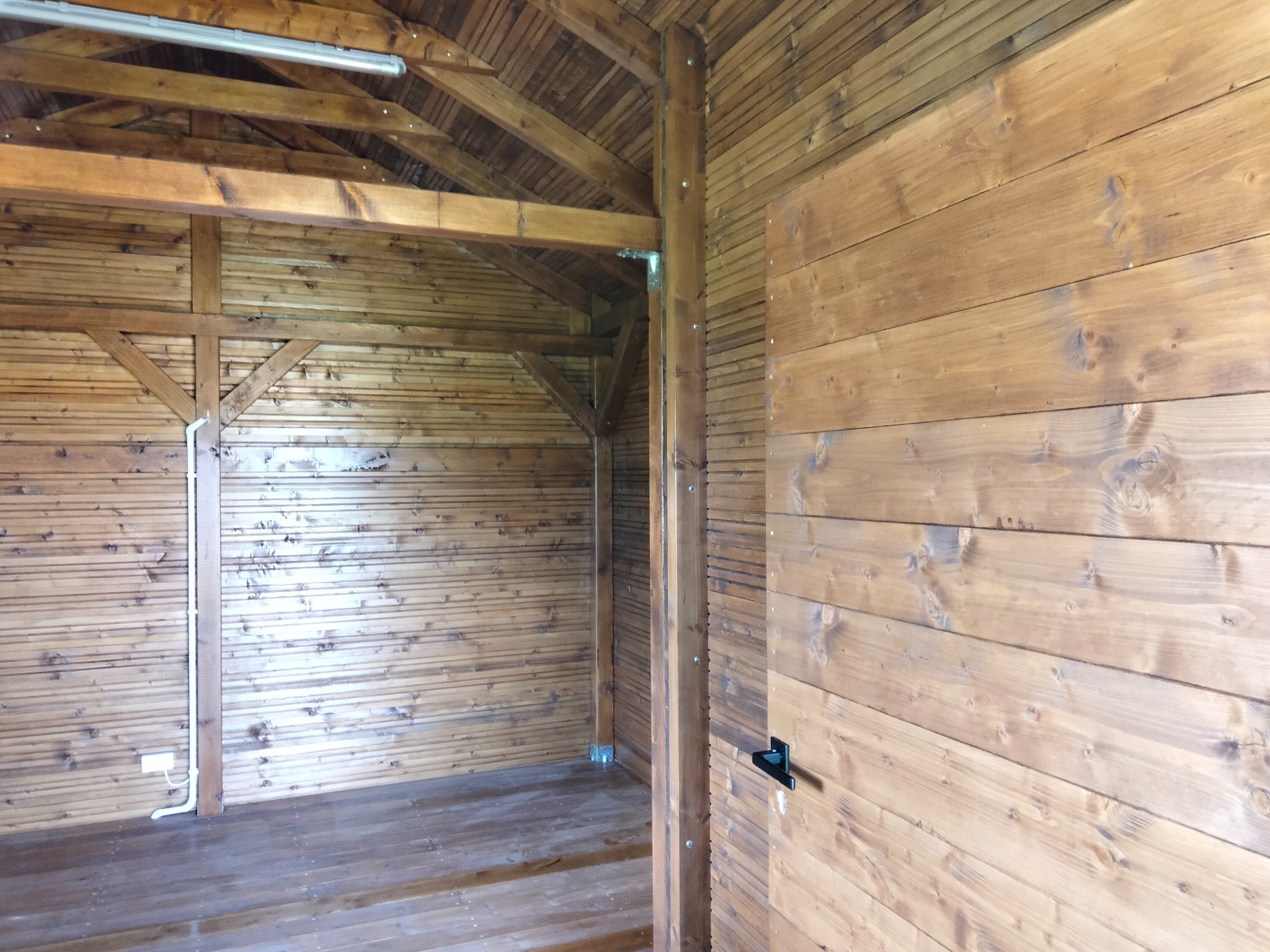 Wnętrze drewnianej konstrukcji szkieletowej z widocznymi elementami nośnymi, deskami boazeryjnymi i podłogą. Widoczne detale wykończeniowe i oświetlenie.