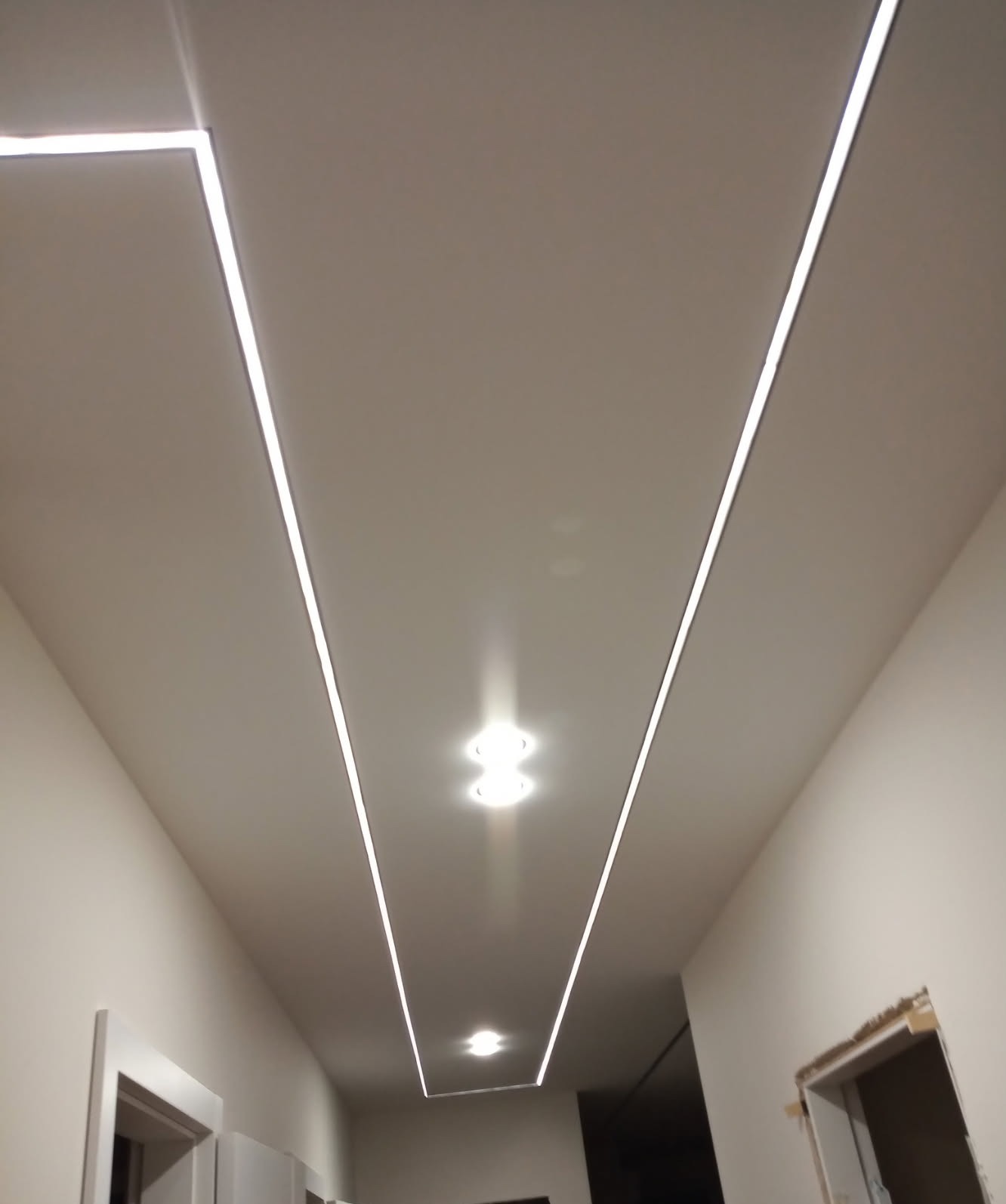 Nowoczesny sufit z liniowym oświetleniem LED w korytarzu. Dwa punkty świetlne. Minimalistyczny design, jasne ściany. Widok z dołu.