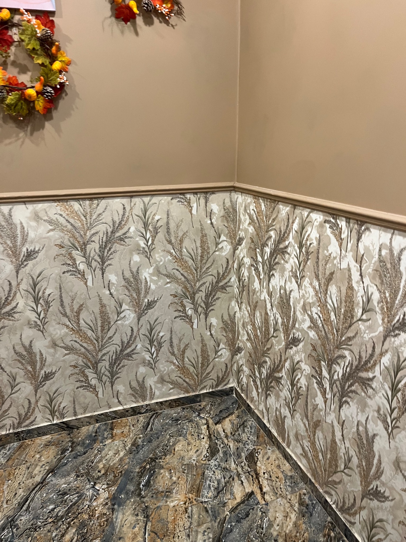 Wnętrze z tapetą w motywy roślinne i marmurową posadzką. Dekoracyjny wieniec na ścianie dodaje ciepła. Ujęcie z narożnika, podkreślające wzór tapety.