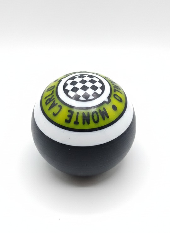Kula z nadrukiem szachownicy i napisem 'Monte Carlo' w kolorze zielonym, czarno-białe paski, czarne dno. Produkt wykonany metodą druku 3D.