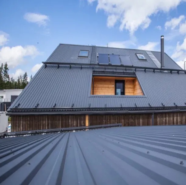 Szary dach z blachy trapezowej z oknami dachowymi i panelami solarnymi, widok z góry na fragment dachu, drewniana elewacja pod dachem.