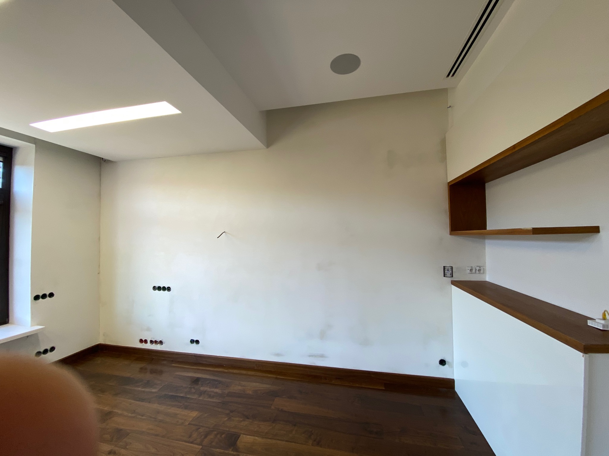 Wnętrze pokoju z drewnianą podłogą i białymi ścianami w trakcie przygotowania do malowania. Widoczne ślady po szpachlowaniu i gniazdka elektryczne.