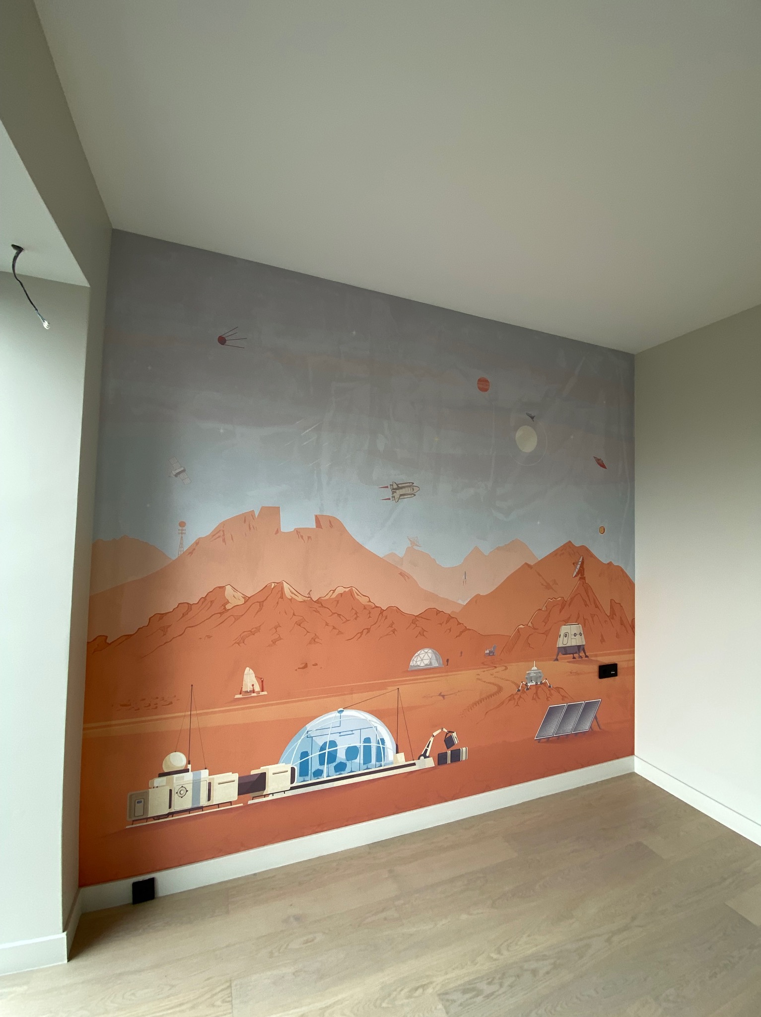 Pokój z fototapetą przedstawiającą krajobraz Marsa z futurystycznymi budowlami i pojazdami. Jasna podłoga i białe ściany tworzą nowoczesne wnętrze.