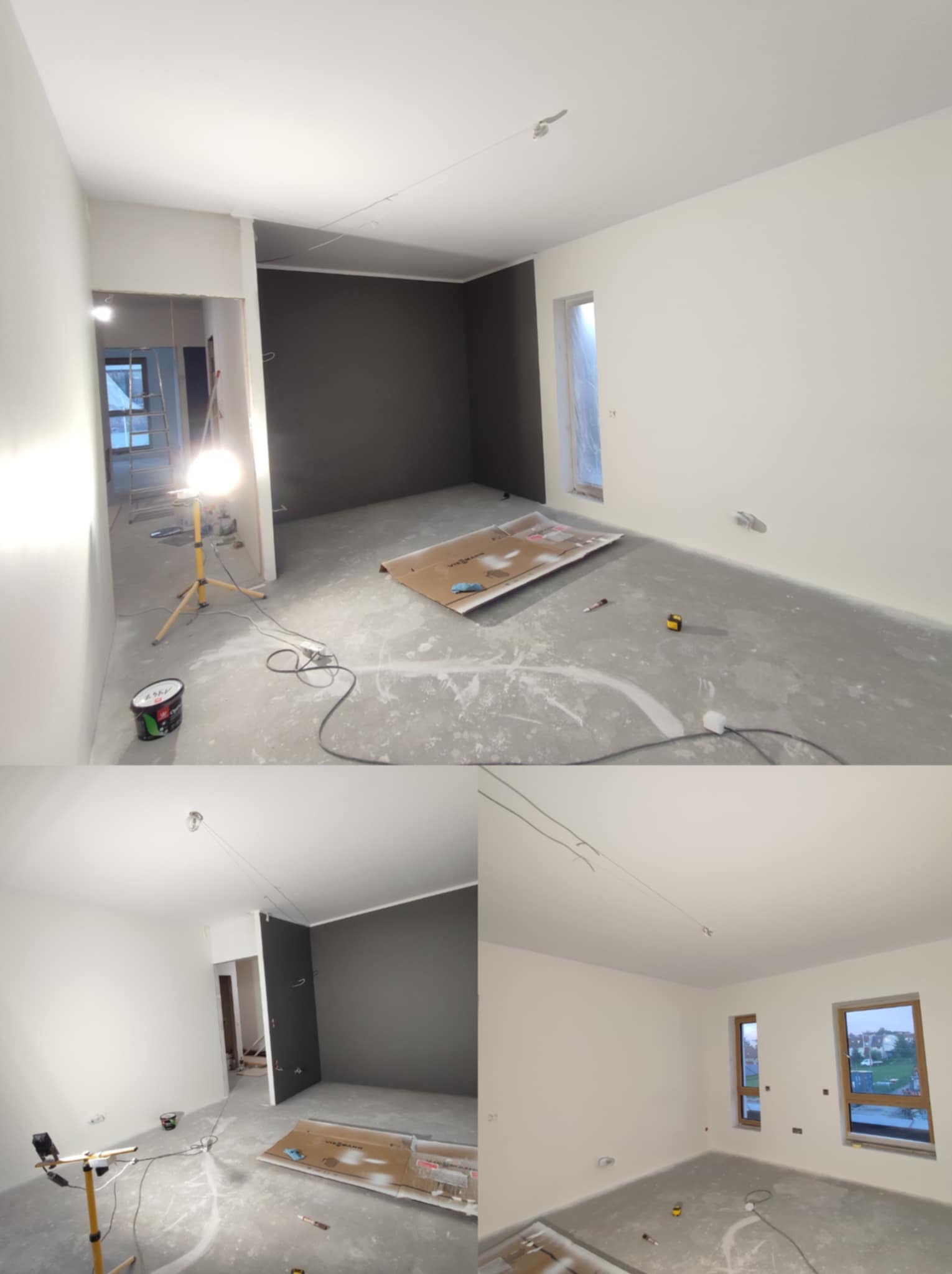 Wnętrze po malowaniu: białe ściany, jedna ściana grafitowa, widoczna lampa budowlana, kartony na podłodze. Dwa okna z widokiem na zewnątrz.