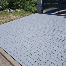 Clean-Mar Wiesław Śliwa - Świeżo pomalowana na szaro kostka brukowa przed posesją z czarną bramą, widoczne ślady farby na fugach. W tle zieleń i zabudowania.
