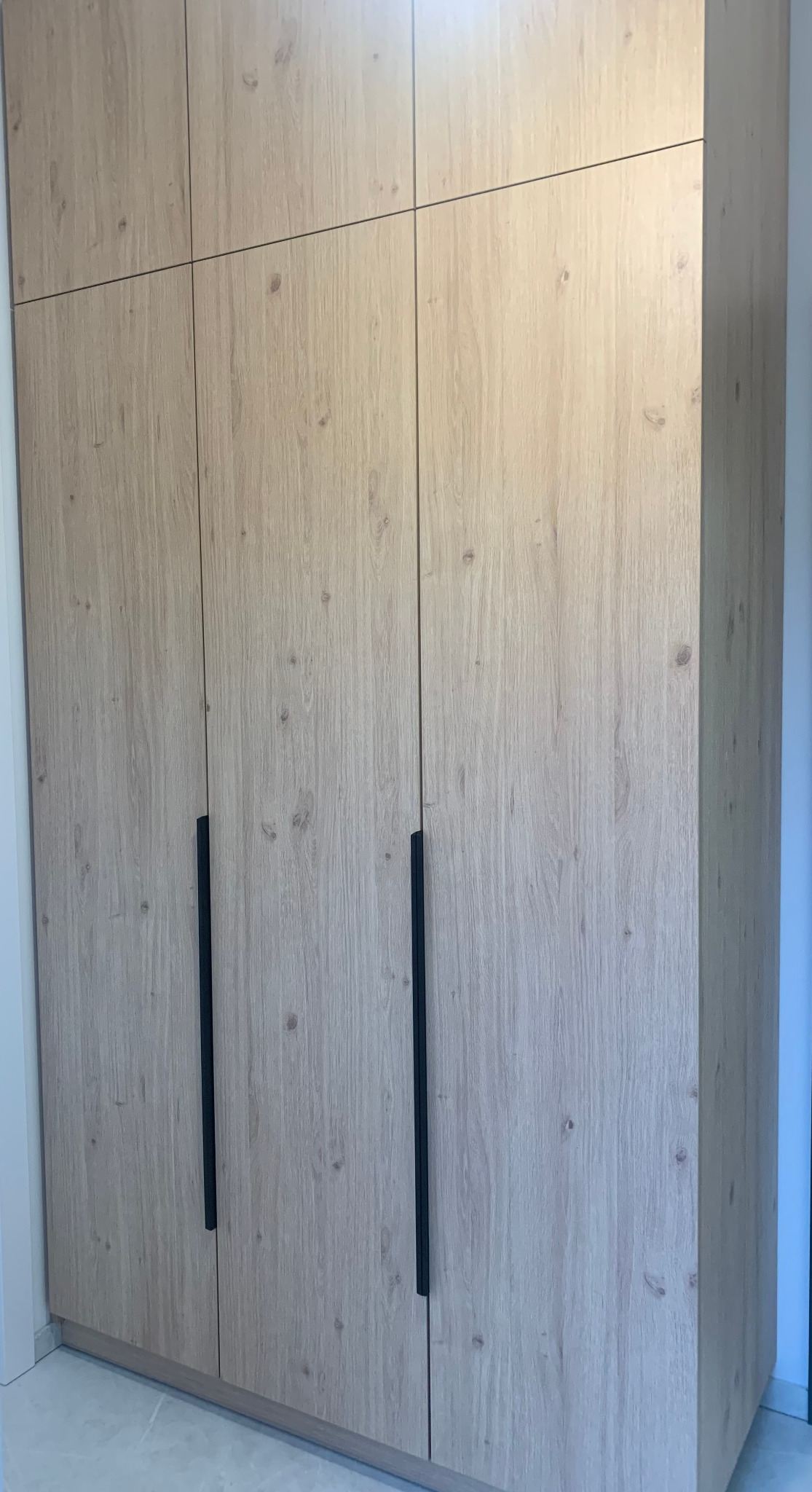 Jasna, drewnopodobna szafa na wymiar z czarnymi uchwytami, wykonana we Wrocławiu. Minimalistyczny design, widoczne łączenia paneli.