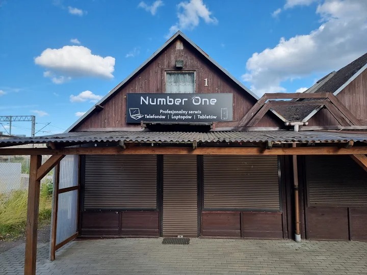 Fasada budynku z szyldem 'Number One': profesjonalny serwis telefonów, laptopów i tabletów. Zamknięte rolety, drewniana konstrukcja, błękitne niebo z chmurami w tle.