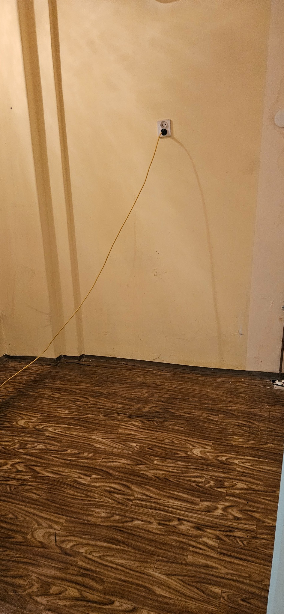 Ukończona podłoga z paneli imitujących drewno, widoczna ściana z gniazdkiem i wystającym kablem. Ujęcie z niskiego kąta, podkreślające wzór podłogi.