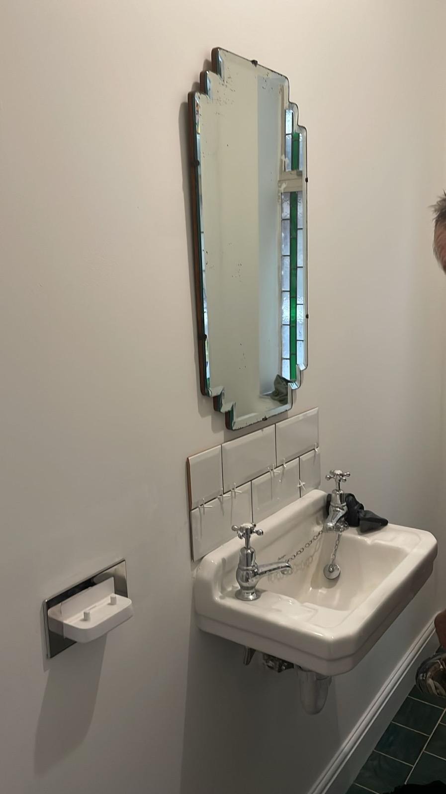 Biała umywalka z baterią retro i lustrem art deco na ścianie z nowo ułożonymi białymi płytkami. Widoczne krzyżyki dystansowe.