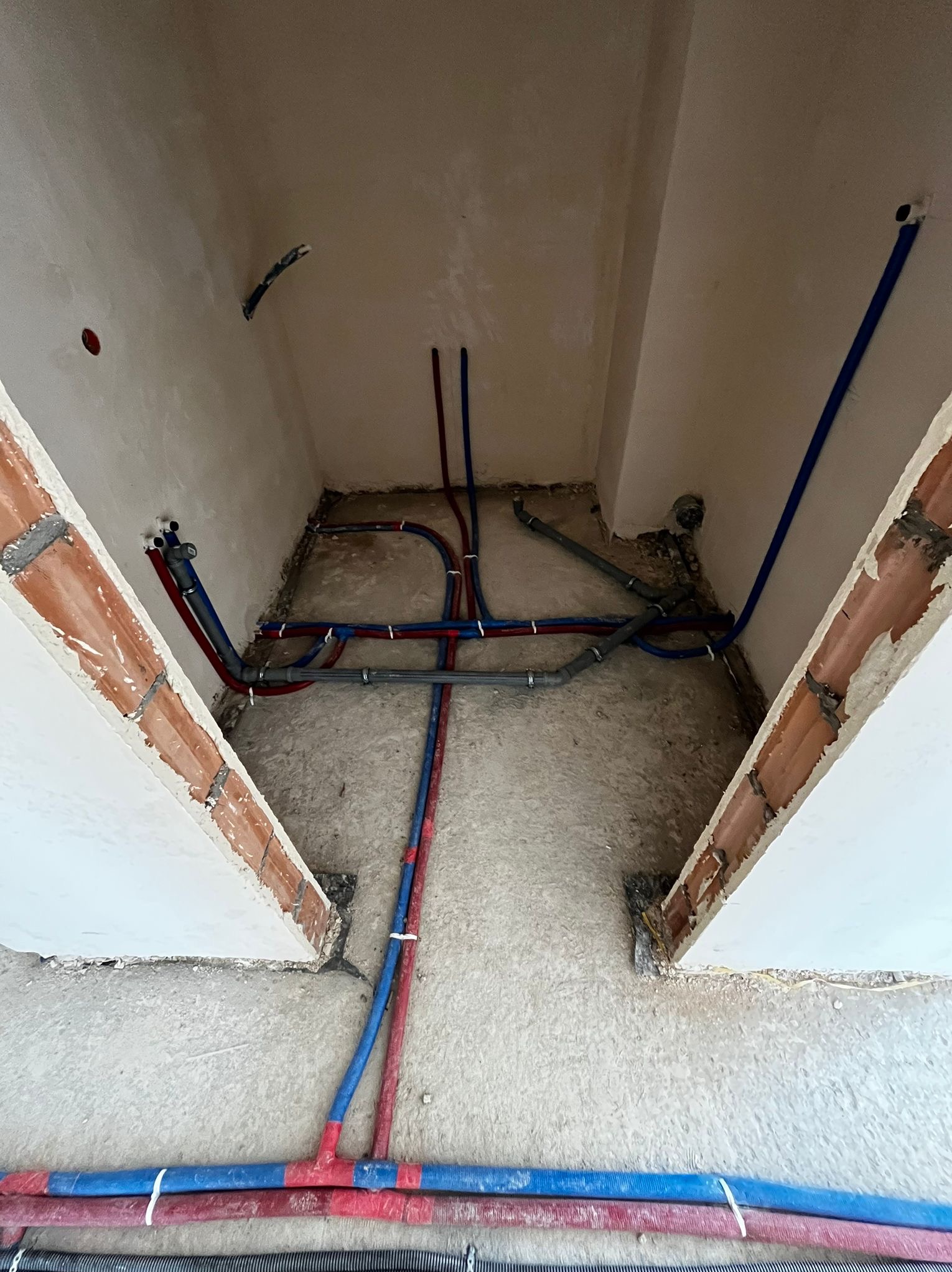 Rozbudowana instalacja wodno-kanalizacyjna z rurami PEX w kolorach niebieskim i czerwonym, zamontowana w surowym pomieszczeniu z ceglanymi elementami konstrukcyjnymi.