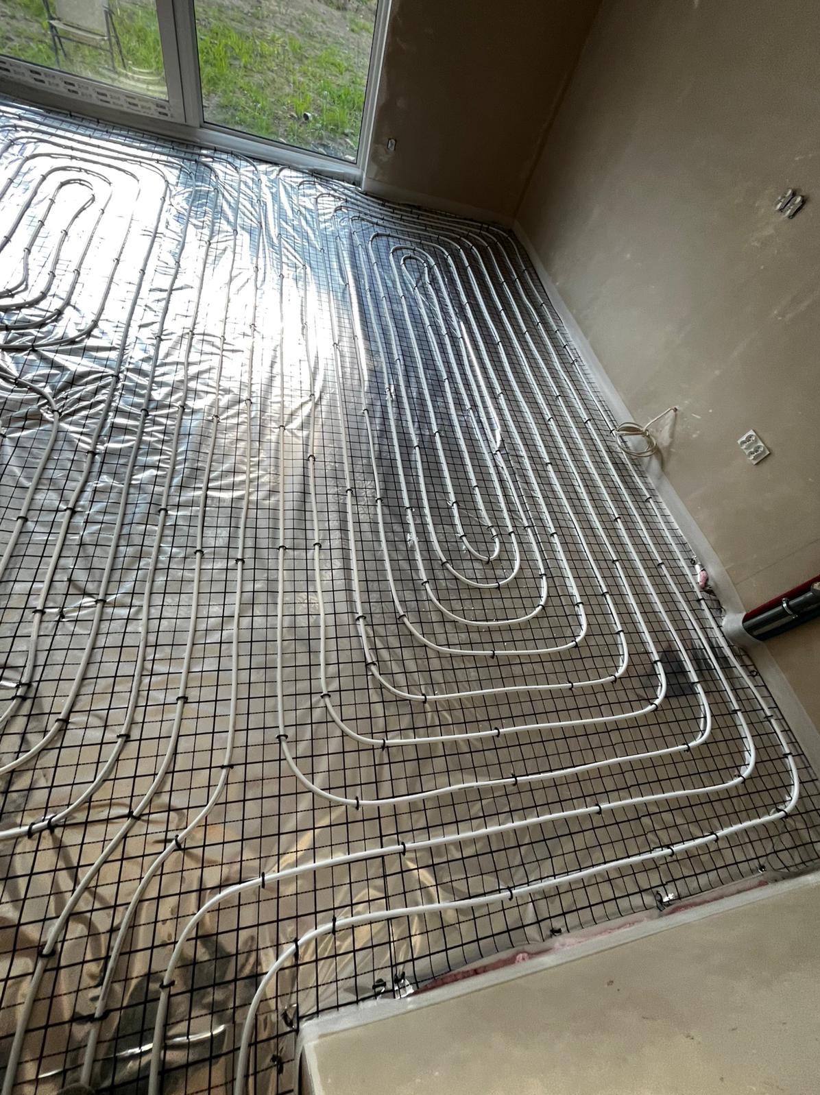 Białe rury ogrzewania podłogowego ułożone na folii i siatce w jasnym pomieszczeniu z oknem. Widok z góry, ukośny kadr.