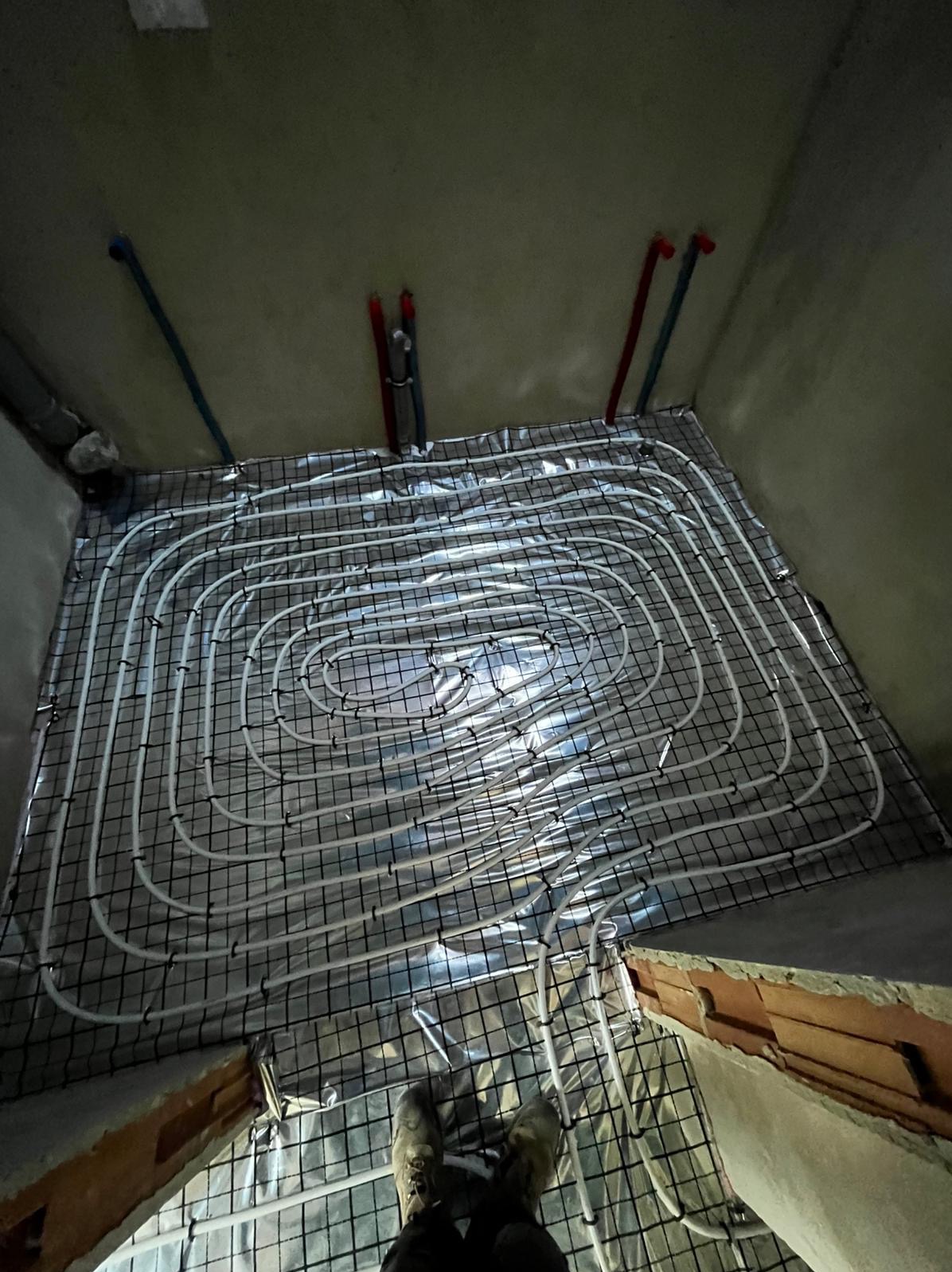 Białe rury ogrzewania podłogowego na folii, zamocowane do siatki, widok z góry, Rzyki. Elementy instalacji grzewczej w surowym wnętrzu.