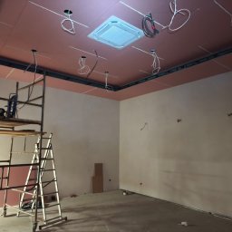 Global Elektro Grzegorz Duda, Łukasz Gołdyn Spółka Cywilna - Wnętrze w trakcie prac: podwieszany sufit z klimatyzacją, wystające przewody elektryczne, rusztowanie. Widoczne przygotowania do instalacji oświetlenia.