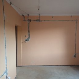 Global Elektro Grzegorz Duda, Łukasz Gołdyn Spółka Cywilna - Wnętrze w trakcie prac elektrycznych: kable prowadzone po ścianach i suficie, zabezpieczone gipsem. Widoczne puszki instalacyjne i fragment narzędzia na podłodze.