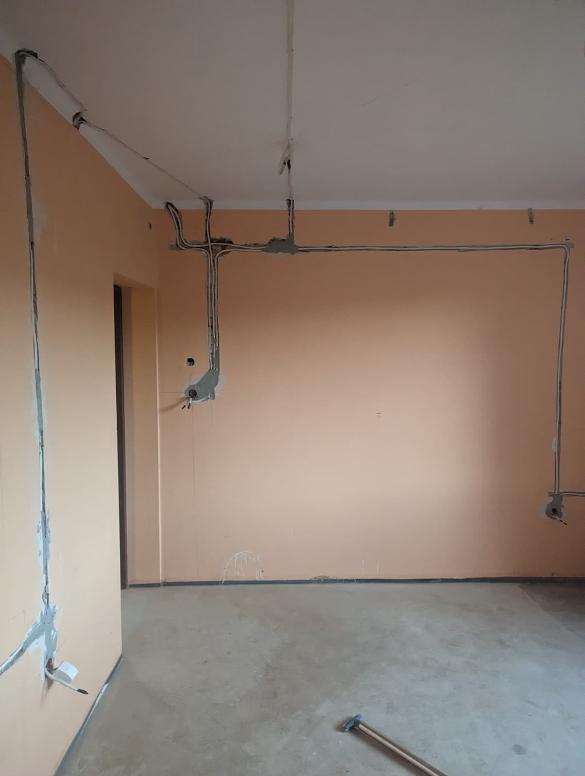 Wnętrze w trakcie prac elektrycznych: kable prowadzone po ścianach i suficie, zabezpieczone gipsem. Widoczne puszki instalacyjne i fragment narzędzia na podłodze.