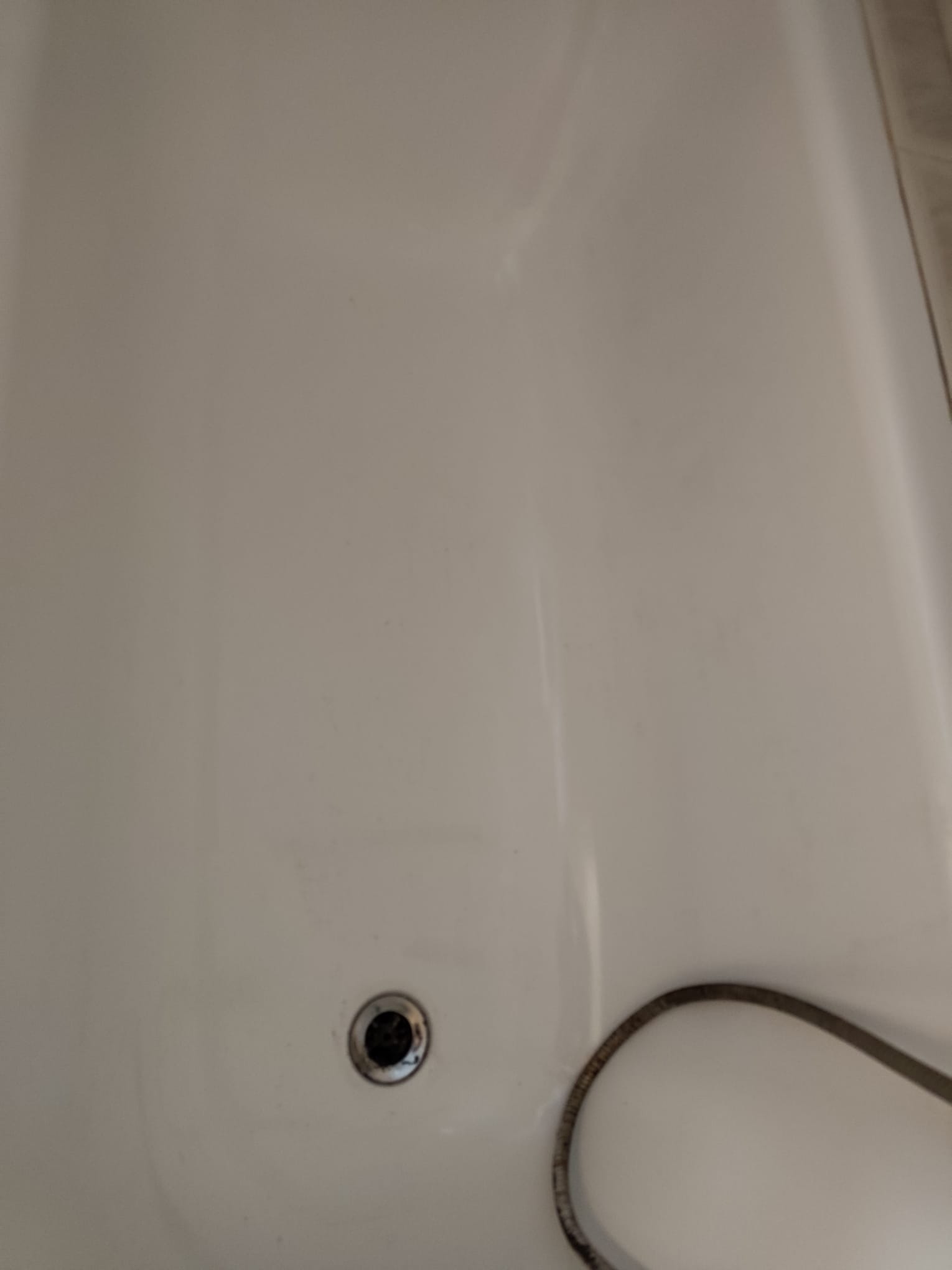 Biała wanna z widocznym odpływem i fragmentem węża prysznicowego. Minimalistyczne ujęcie, skupiające się na czystości i detalu armatury.