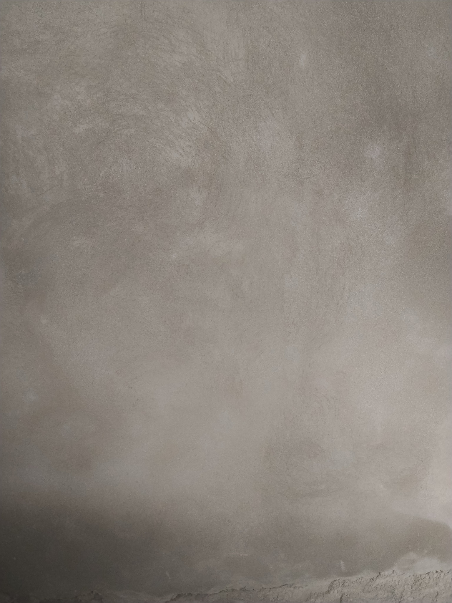 Gładka, szara powierzchnia ściany po nałożeniu tynku. Widoczne delikatne, nieregularne wzory i faktura. U dołu ściany widoczne drobne nierówności.