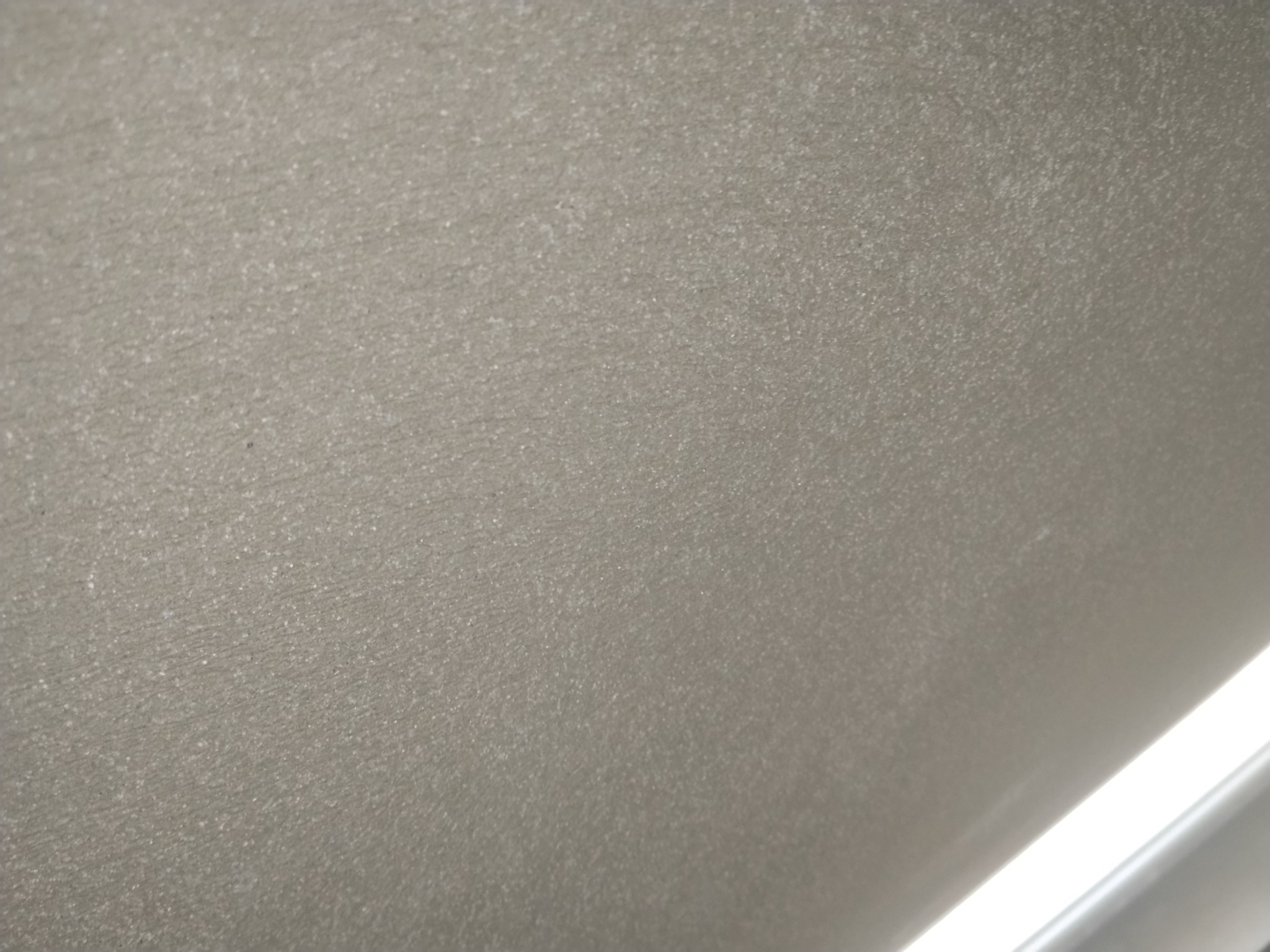 Gładka, szara powierzchnia ściany z delikatną fakturą, oświetlona od dołu, ukazująca precyzję wykonania i równomierne pokrycie.