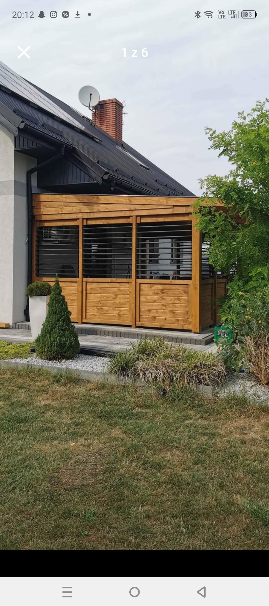 Drewniana zabudowa tarasu z żaluzjami w nowoczesnym stylu, przylegająca do domu. Uwagę zwraca jasne drewno i minimalistyczny design, wkomponowany w otoczenie ogrodu.