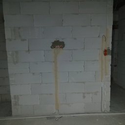 INSTAL-KAM Karol Kamiński - Ściana z betonu komórkowego z widocznymi puszkami elektrycznymi i przewodami, przygotowana do dalszych prac instalacyjnych wewnątrz budynku.