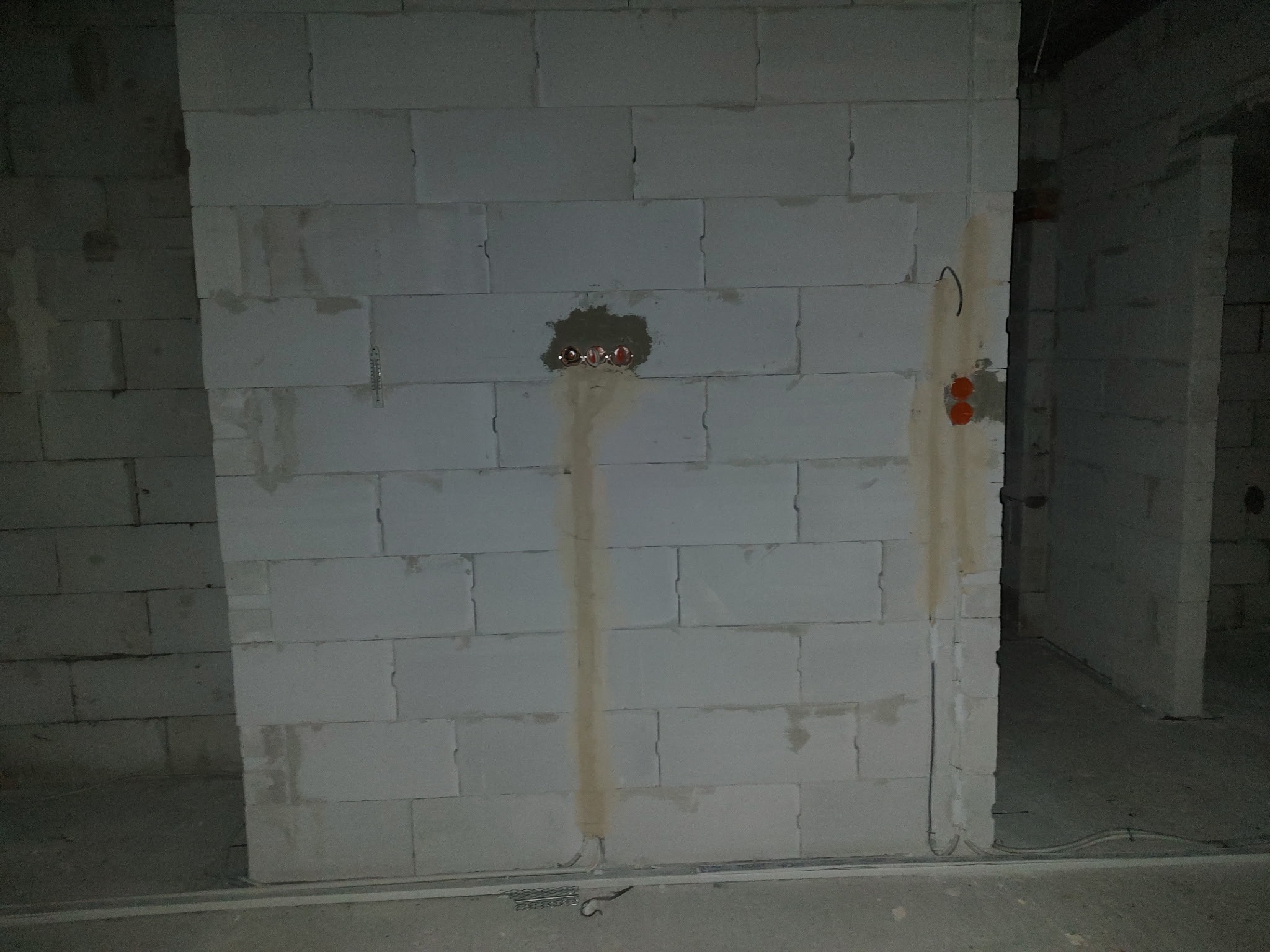 Ściana z betonu komórkowego z widocznymi puszkami elektrycznymi i przewodami, przygotowana do dalszych prac instalacyjnych wewnątrz budynku.