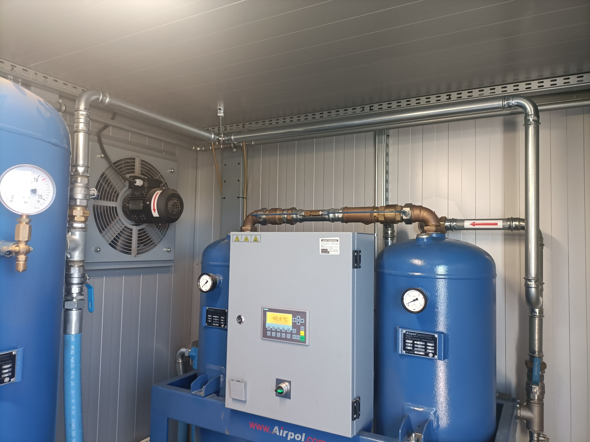 Kompresorownia Airpol z niebieskimi zbiornikami, szarą obudową sterowniczą i wentylatorem. Widoczne rury, manometry i panel sterowania z wyświetlaczem.