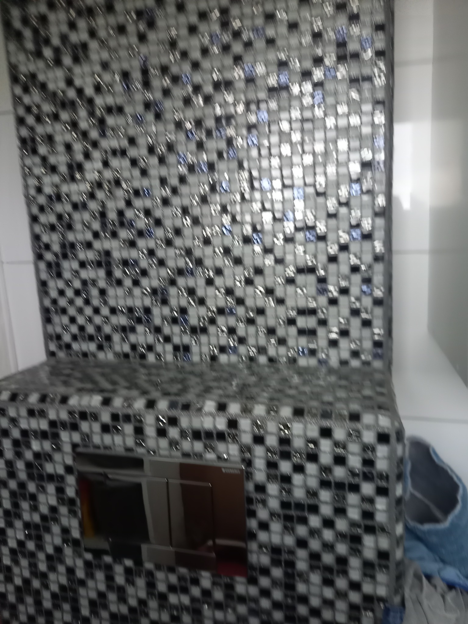 Mozaika w odcieniach szarości i bieli zdobi zabudowę toalety podtynkowej z chromowanym przyciskiem spłukującym. Element wystroju łazienki po remoncie.