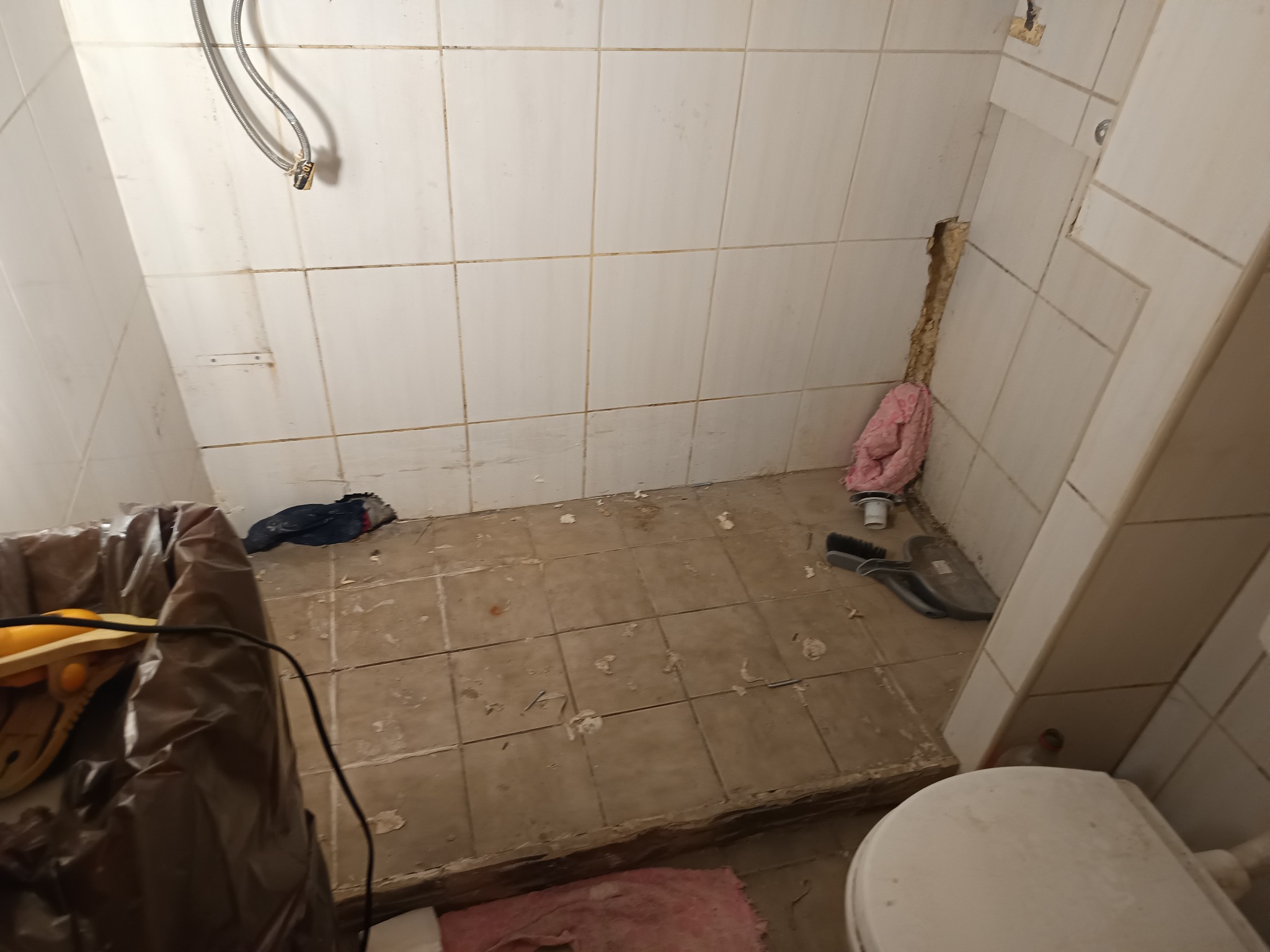 Łazienka w trakcie demontażu płytek, widoczny fragment toalety, ślady po kleju, narzędzia i śmieci. Przygotowanie do remontu.