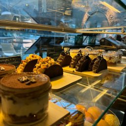 AP events - Witryna cukiernicza z deserami: tiramisu, tartaletki z kremem i ciastka w słoiczkach. W tle widoczne odbicie wnętrza kawiarni.