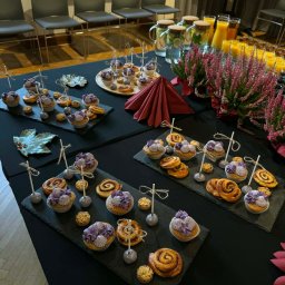 AP events - Elegancki stół z cateringiem: babeczki z fioletowym kremem, cynamonki, napoje w dzbankach i dekoracje z wrzosu, tworzące wyrafinowaną kompozycję.