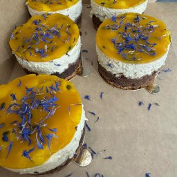 AP events - Cztery mini torty z musem, galaretką z marakui i dekoracją z niebieskich kwiatów w kartonowym pudełku. Widok z góry, delikatne światło.