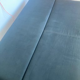 Król Kanapy - Ciemnoszara, rozłożona kanapa z widocznym szwem, ustawiona przy białej ścianie i drewnianej szafce. Ujęcie z góry, prezentujące czystą tapicerkę.