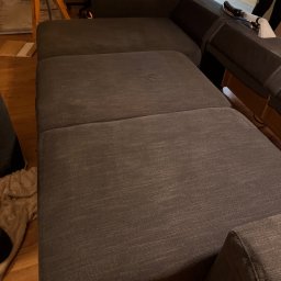 EDISON PRO CLEAN - Ciemnoszara, rozłożona sofa modułowa z widoczną końcówką węża do prania tapicerki, sugerująca etap czyszczenia. Ujęcie z bliska, w tle fragmenty mebli.
