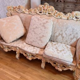 EDISON PRO CLEAN - Elegancka, beżowa kanapa w stylu Ludwika z dekoracyjnymi, złoconymi elementami i wzorzystą tapicerką, ustawiona na parkiecie. Widoczny fragment stolika nocnego w tle.