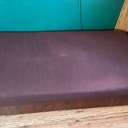 EDISON PRO CLEAN - Fioletowa kanapa z drewnianą ramą na parkiecie, na tle turkusowej ściany i zasłony w liście. Widoczne ślady użytkowania na tapicerce.